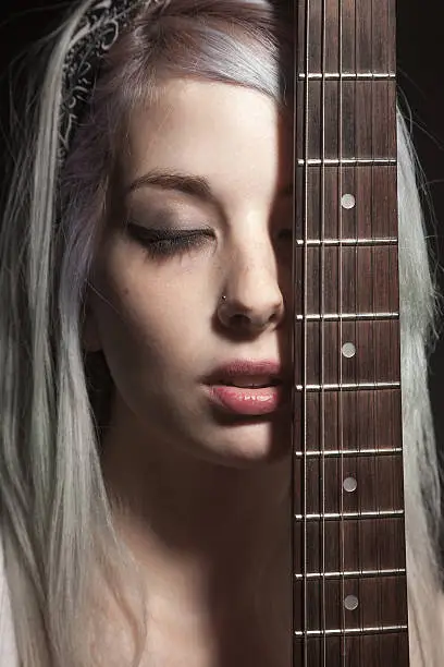 Close-up portrait of a young woman covering her face with a electric guitar fretboard.