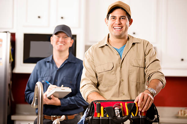 Service Industry: Two multi-ethnic repairmen work at customer's home. Caucasian and Hispanic repairmen or blue collar/service industry workers make service/house call at customer's home kitchen. One holds his tool box filled with work tools. Other worker holds a clipboard in background.  Inspector, exterminator, electrician, plumber, repairmen.   electrician smiling stock pictures, royalty-free photos & images