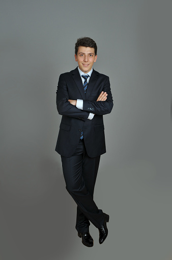 Portrait of teenage boy in suit against gray background. Young man standing in front of gray background and posing to camera. Vertical shot. Image taken in studio and developed from Raw format.