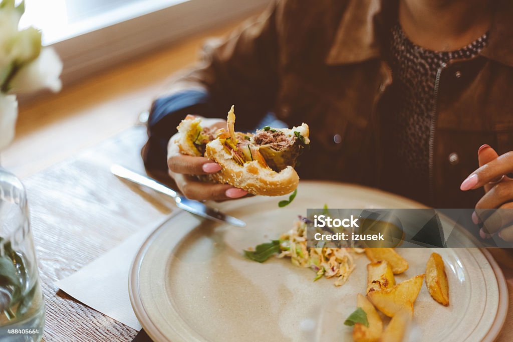 Afro american woamn eating burger in a restaurant Afro american woman eating burger in the restaurant. Focus on hands. Unrecognizable person.  2015 Stock Photo