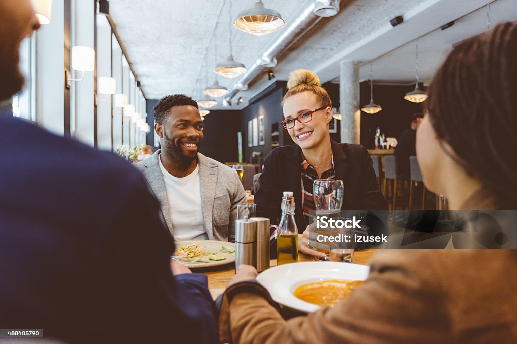 Multi ethnic group of friends eating dinner in a restaurant Multi ethnic group of happy friends - caucasian and afro american - eating dinner in the restaurant. Blonde woman wearing nerd glasses drinking beer. Restaurant Stock Photo
