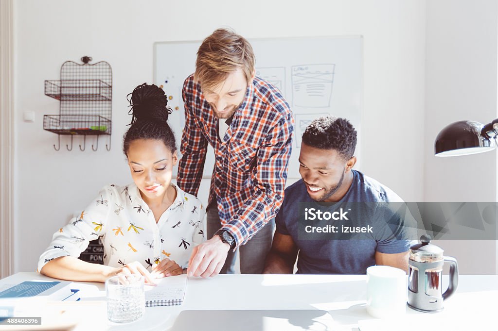 Multi ethnic team working in an office together Start-up or advertising agency. Multi ethnic team - caucasian and afro american - working together in an office. 2015 Stock Photo