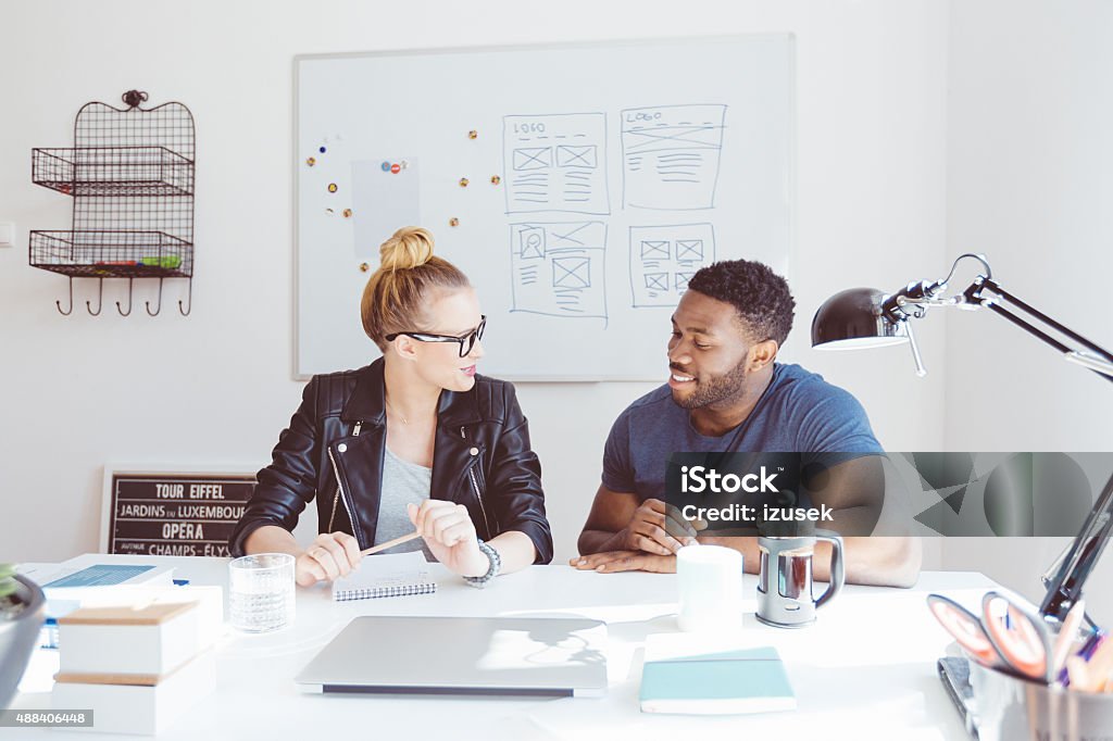 Blonde woman talking with afro american colleague in office Start-up or advertising agency. Blonde woman and afro american man discussing in an office.  2015 Stock Photo