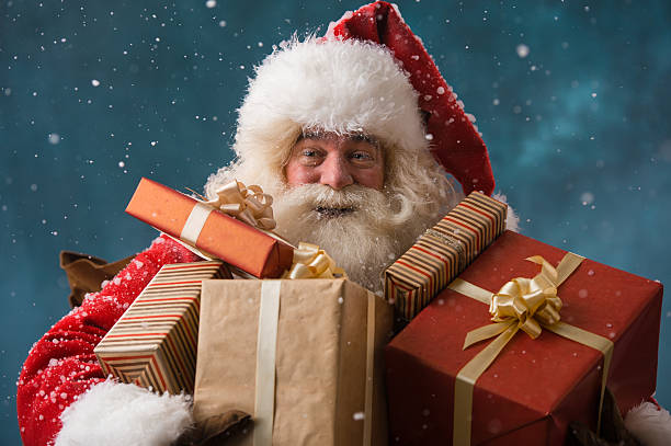 Photo of happy Santa Claus outdoors in snowfall carrying gifts stock photo