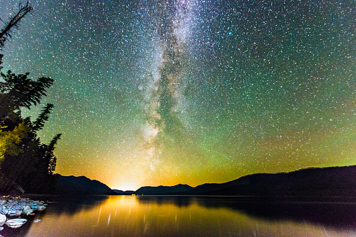 This is a horizontal, color, royalty free stock photograph of the night sky landscape in Glacier National Park. Dark mountains and trees are back lit with the night sky. Northern lights and the Milky Way are visible above Lake McDonald. Photographed with a Nikon D800 DSLR camera.