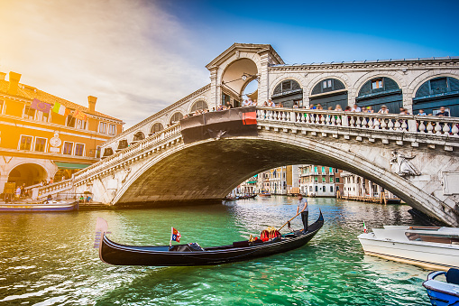 Beautiful view of traditional Gondola on famous Canal Grande with Rialto Bridge at sunset in Venice, Italy with retro vintage Instagram style filter and lens flare effect.