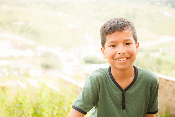 Asian, Indian descent young boy standing outdoors on a hill.   The happy elementary age boy is wearing a green shirt.  Villages in northeastern India can be seen in the background in the valleys.   Copyspace.