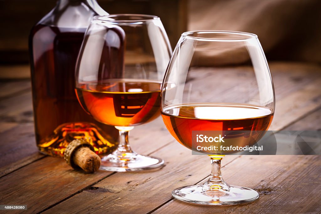 Cognac snifters with bottle on rustic wood table Front view of two cognac snifters and a open cognac bottle shot on rustic wood table. Low key DSRL studio photo taken with Canon EOS 5D Mk II and Canon EF 70-200mm f/2.8L IS II USM Telephoto Zoom Lens Cognac - Brandy Stock Photo