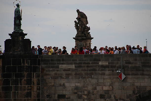 Prague, Сzech Republic - August 20, 2014: The Charles Bridge is a famous historic bridge that crosses the Vltava river in Prague, Czech Republic. Its construction started in 1357 under the auspices of King Charles IV, and finished in the beginning of the 15th century. As the only means of crossing the river Vltava (Moldau) until 1841, the Charles Bridge was the most important connection between Prague Castle and the city's Old Town and adjacent areas. The bridge is 621 m long and nearly 10 m wide, resting on 16 arches shielded by ice guards. It is protected by three bridge towers, two of them on the Lesser Quarter side and the third one on the Old Town side. The Old Town bridge tower is often considered to be one of the most astonishing civil gothic-style buildings in the world. The bridge is decorated by a continuous alley of 30 statues and statuaries, most of them baroque-style, originally erected around 1700 but now all replaced by replicas.