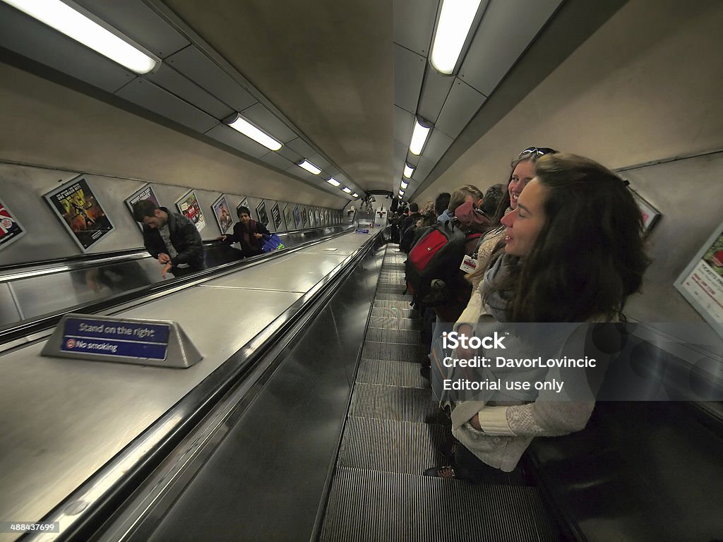 Metro Elevator London, United Kingdom - October 30, 2013:Detail in the Metro. People are standing on escalator and riding up from deep in ground. In background are light lines and commercial panels, which hang on the wall. Adult Stock Photo