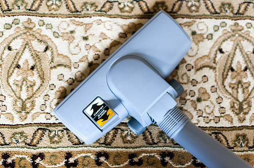 A close-up of a vacuum cleaner, that is capable of cleaning both hardwood and carpeted floors.  The vacuum is cleaning an oriental rug.