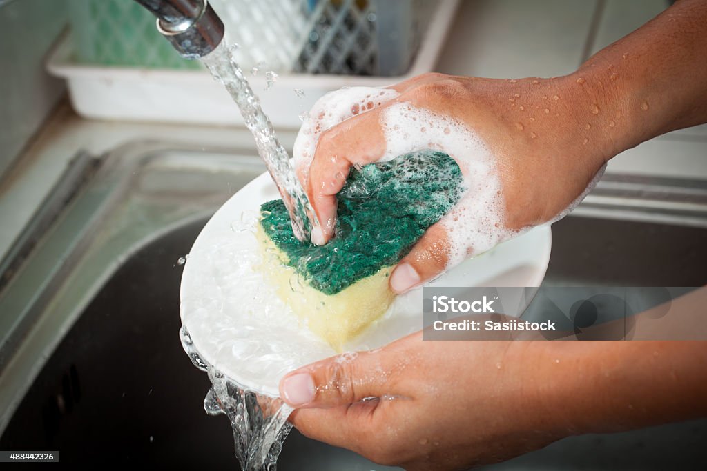 Woman hand washing dishes over the sink in the kitchen Washing Stock Photo