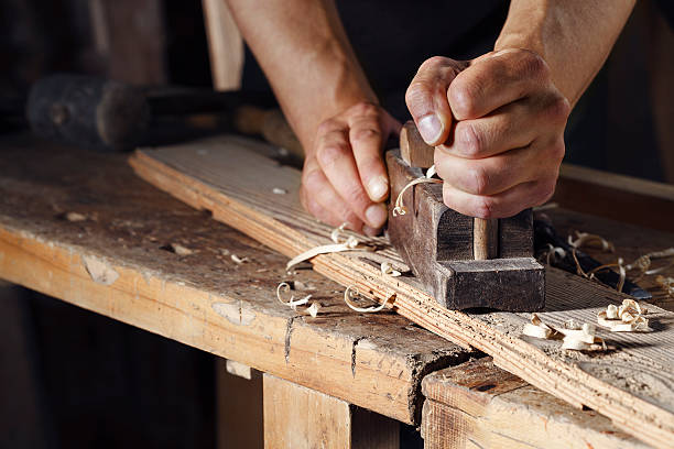 carpenter planing a plank of wood with a hand plane Close up of a carpenter planing a plank of wood with a hand plane plane hand tool photos stock pictures, royalty-free photos & images