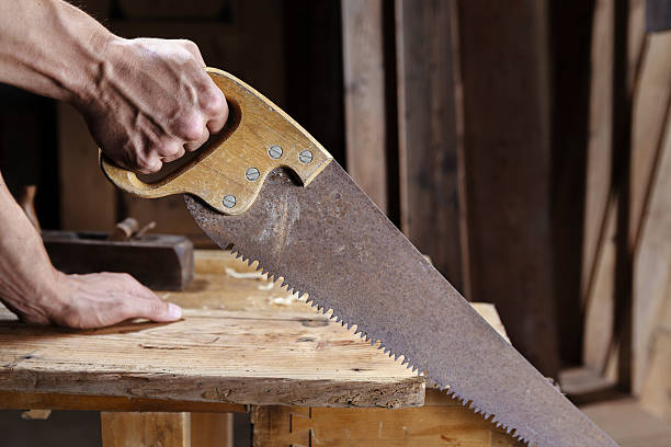 Carpenter sawing a board with a hand wood saw stock photo