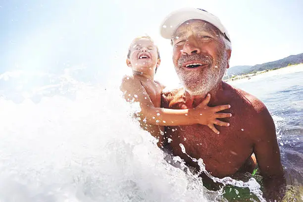 Photo of smiling grandfather and his little grandson having fun bathing in the sea