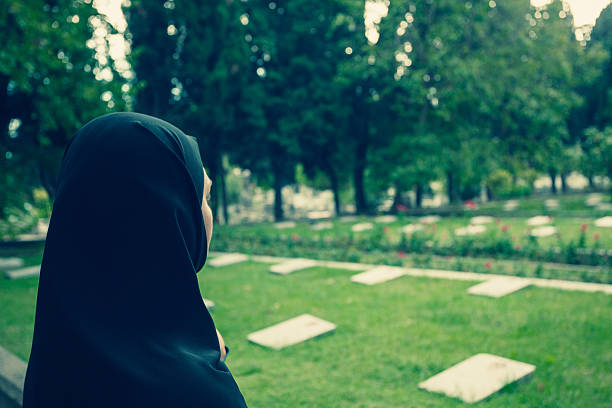 one mature adult woman standing at grave of old graveyard on day in autumn, shallow focus on person, stone of tomb blurred in foreground