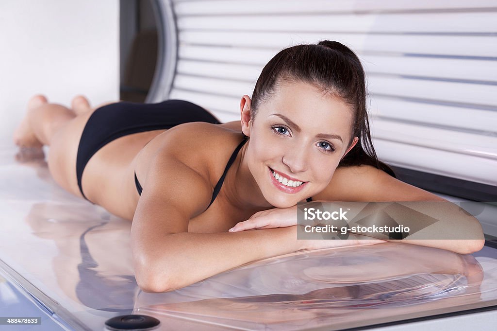 Beautiful woman in solarium. Attractive young woman tanning in solarium and smiling at camera Tanning Bed Stock Photo