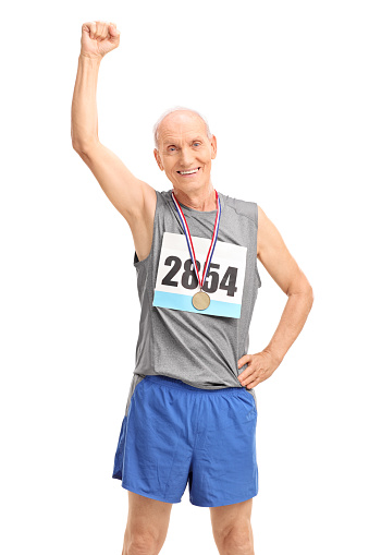 Vertical shot of a mature runner with a medal raising his fist in the air and looking at the camera isolated on white background
