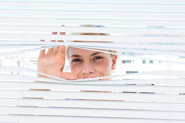 istock Curious blonde woman looking through venetian blind 488488606