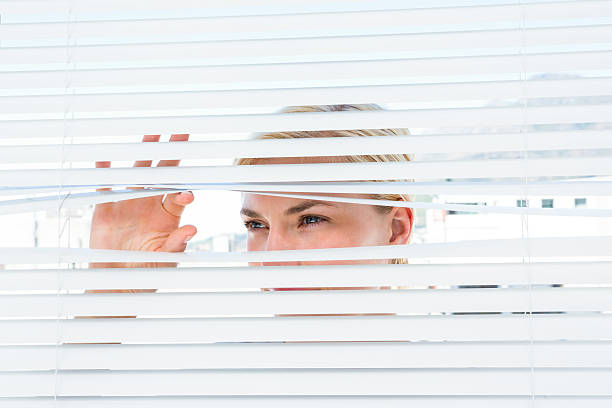 istock Curious blonde woman looking through venetian blind 488488622