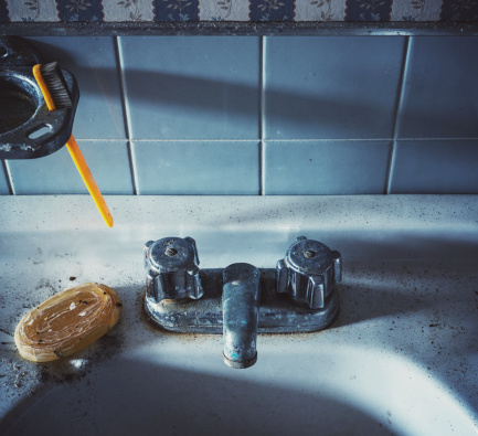 A dirty bathroom sink with old toothbrush and dried bar of soap.