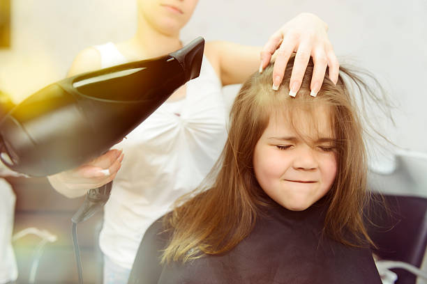 drying hair little girl expressing negativity at hairdresser drying her hair. angry hairstylist stock pictures, royalty-free photos & images