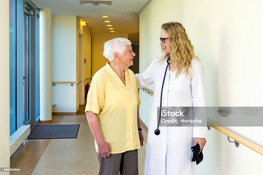 Doctor chatting to an elderly lady patient. Attractive female doctor chatting to an elderly lady patient in a hospital corridor reassuring her with a smile and a hand on her back. 2015 Stock Photo