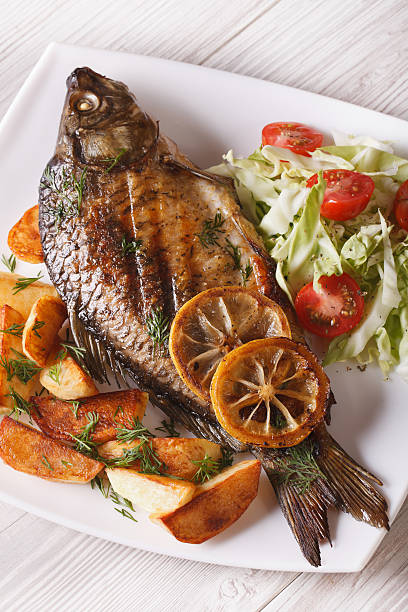 istock grilled fish with fried potatoes and salad vertical top view 488514170
