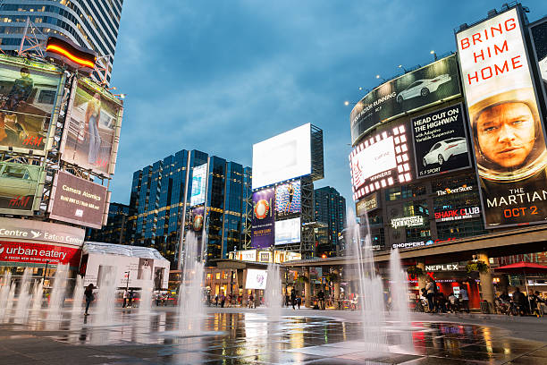 Yonge and Dundas square illuminated at dusk Toronto, Canada - September 12, 2015: People shopping and relaxing at Yonge and Dundas Square in Toronto at dusk, illuminated by the lights of the colorful neon billboards and advertisements. toronto dundas square stock pictures, royalty-free photos & images