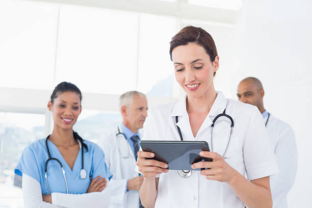 istock Confident female doctor holding tablet with her team behind 488518708