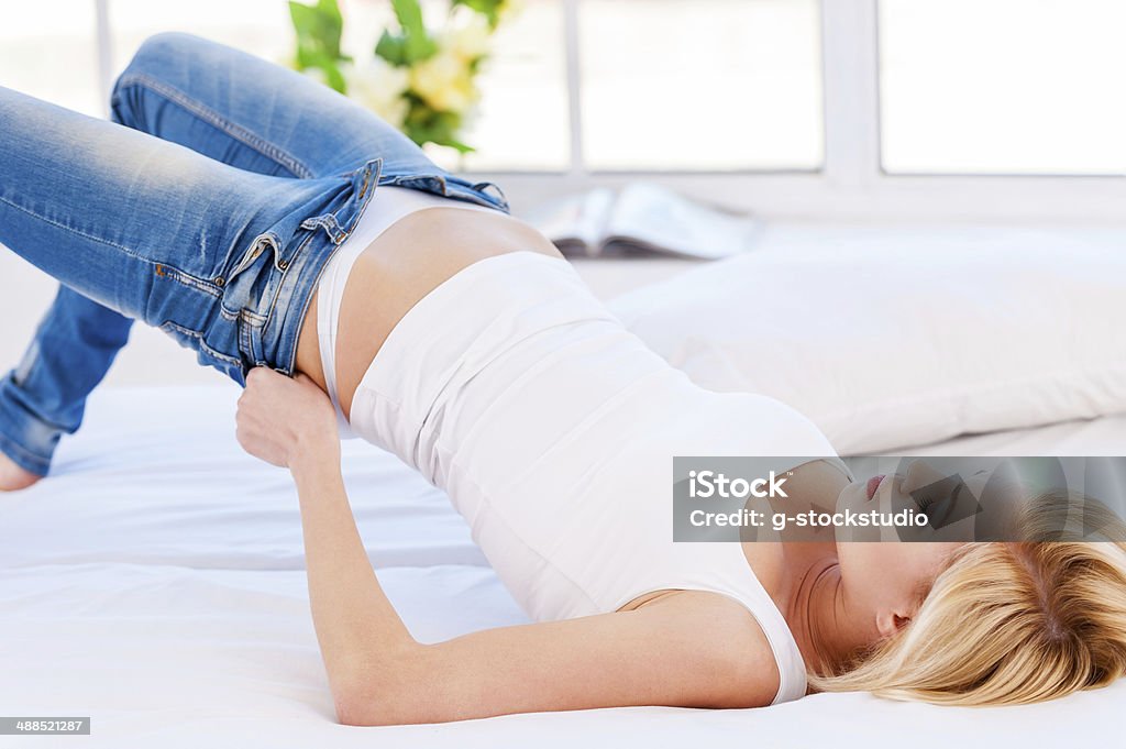 Too tight. Young blond hair woman lying on the bed and pulling on tight jeans Adult Stock Photo