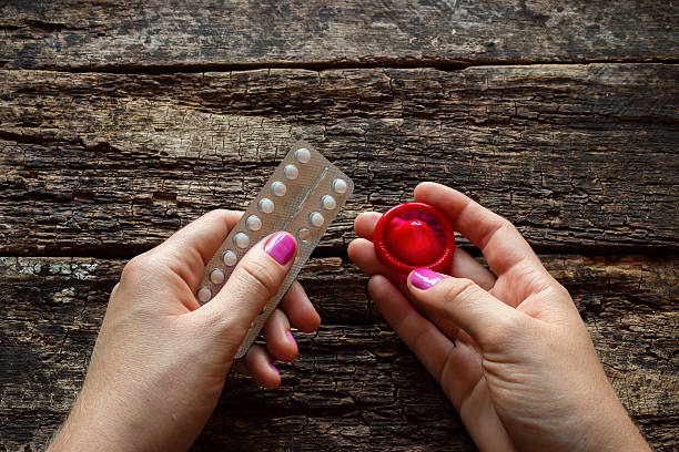 młoda kobieta trzyma z pigułki antykoncepcyjne i prezerwatywa - hiv aids condom sex zdjęcia i obrazy z banku zdjęć