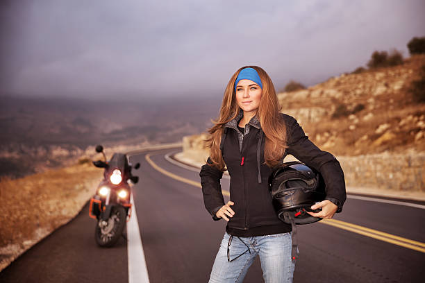 Female biker sitting on motorcycle and putting on gloves while preparing for the ride in the city