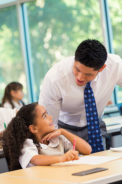 istock Asian male teacher helping student in elementary school classroom 488524040