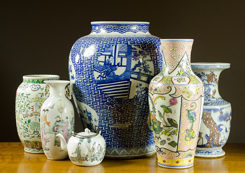 Collection of antique Chinese porcelain vases, urns and teapot.  On a wood table top with black background.