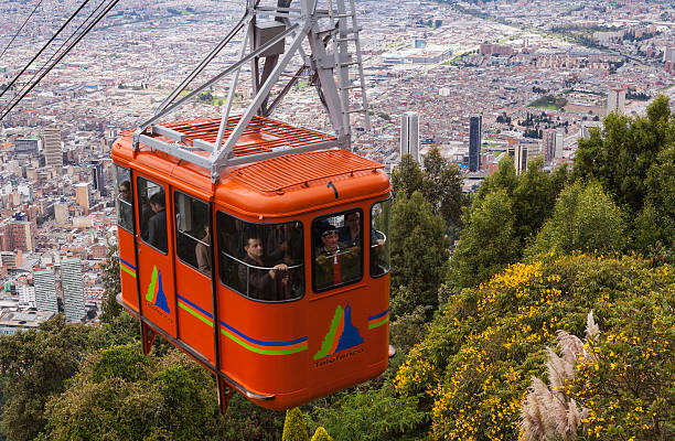 Bogota, Colombia - April 23, 2014: A cable car full of tourists and visitors approaches the Andean peak of Monserrate above the capital city of Bogota in Colombia, South America.  Cables and a pylon can be seen in the background.  The trip up to the peak is popular with visitors and tourists to the city as it has some excellent views of the big Andean city.  The church on top of the peak is also a pilgrimage destination; it draws thousands of pilgrims each month who also use the cable car. Photo shot in the afternoon sunlight; hotizontal format.