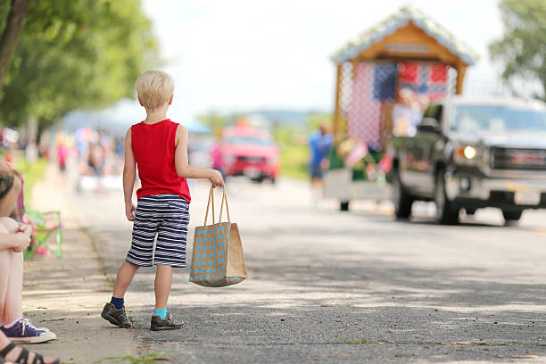 Young Child Watching Small Town America Parade A young boy child standing outside in the summer watching a small town american parade and holding a candy bag. parade stock pictures, royalty-free photos & images