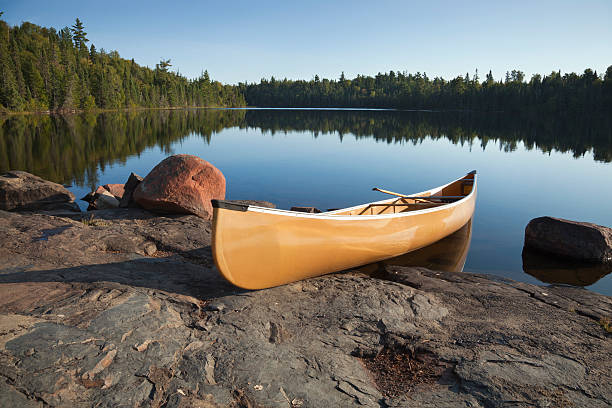 canoe on rocky shore de calma lago de pinos - canoeing canoe minnesota lake fotografías e imágenes de stock