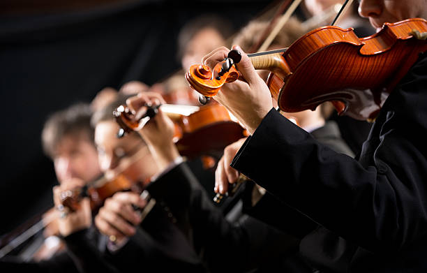 Orchestra first violin section Symphony orchestra first violin section performing on dark background. orchestra stock pictures, royalty-free photos & images
