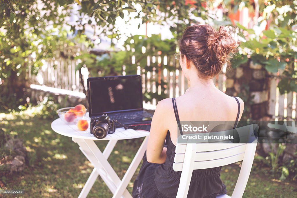 Woman in garden. Attractive woman sitting on chair in garden andworking on laptop. Formal Garden Stock Photo