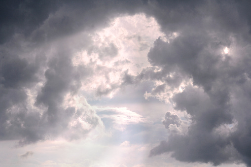 Bright sunlight is peeking between grey cumulonimbus clouds after a thunderstorm in the sky.