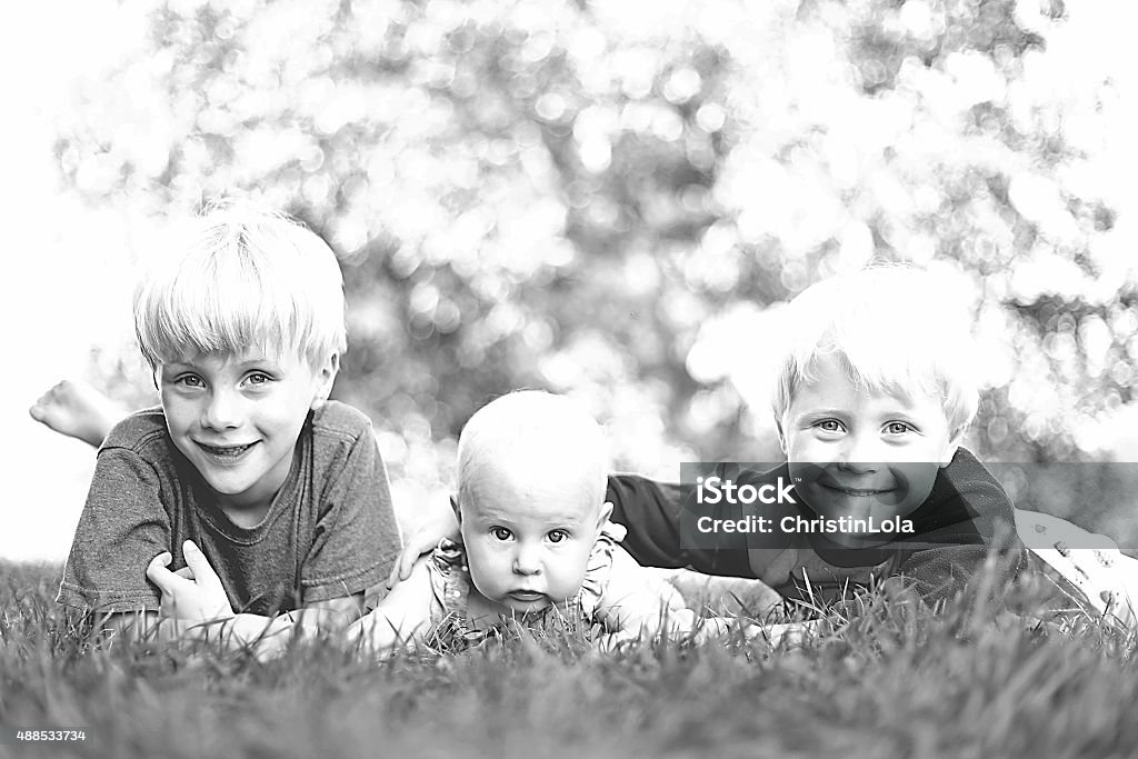 Three Happy Young Children Laughing Outside Three happy young siblings: a young child, his little brother and their baby girl sister are laying outside in the grass on a summer day,  laughing. 12-17 Months Stock Photo
