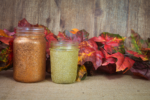 Glitter mason style jars ready to be used as a vase with a fall autumn leaf background.