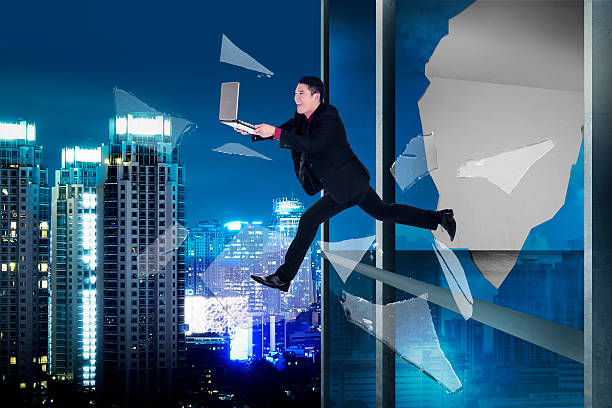 istock Man with laptop jump through office building window 488548210