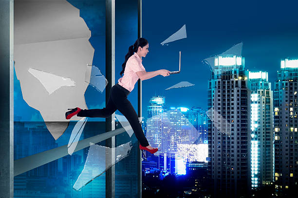 istock Woman with laptop jump through office building window 488548282
