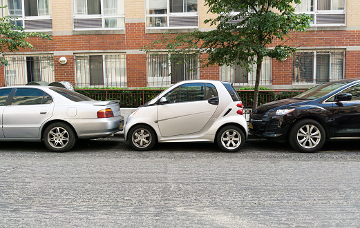 New York City, United States of America - June 10, 2015 - a small car is squashed between two larger cars in a parking space on a street in New York City