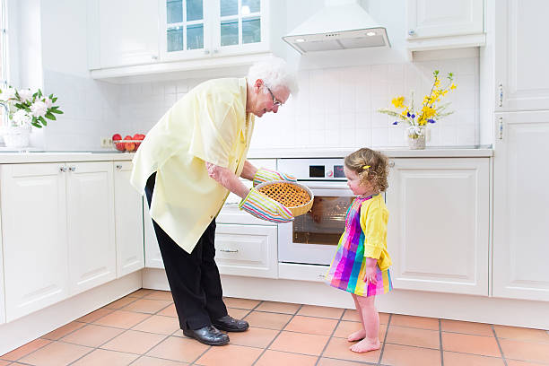 Happy grandmother and little girl baking pie in white kitchen Happy beautiful great grandmother and her adorable granddaughter, curly toddler girl in colorful dress, baking an apple pie together standing next to white oven in sunny modern kitchen with big window fume cupboard stock pictures, royalty-free photos & images
