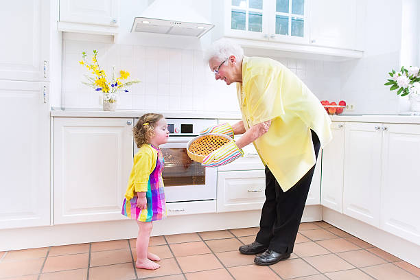 Happy beautiful great grandmother and adorable granddaughter in white kitchen Happy beautiful great grandmother and her adorable granddaughter, curly toddler girl in colorful dress, baking an apple pie together standing next to white oven in sunny modern kitchen with big window fume cupboard stock pictures, royalty-free photos & images