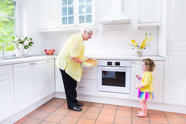 Beautiful grandmother and little girl baking pie in white kitchen Happy beautiful great grandmother and her adorable granddaughter, curly toddler girl in colorful dress, baking an apple pie together standing next to white oven in sunny modern kitchen with big window fume cupboard stock pictures, royalty-free photos & images