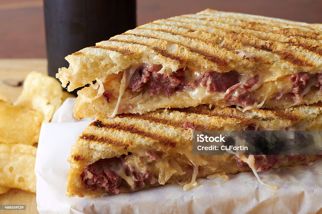 Grilled panini sandwich A gooey meat and cheese sandwich on wax paper with chips and a drink in the background. Panini Stock Photo